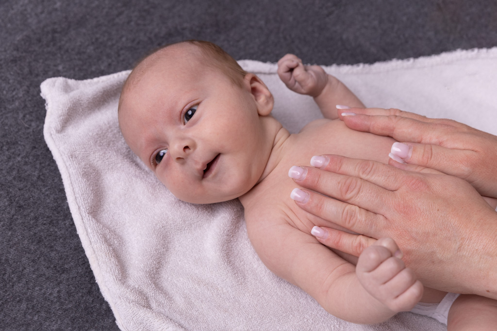 Ein Baby liegt auf dem Rücken, während eine erwachsene Person sanft den Bauch des Babys massiert.